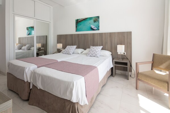 Une chambre d’hôtel moderne avec un grand lit, une tête de lit en bois, une table de chevet avec une lampe et une chaise.