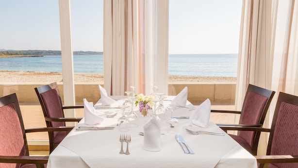 A table set for dining with a view of the beach and ocean. - Hotel Club S'illot (Manacor)
