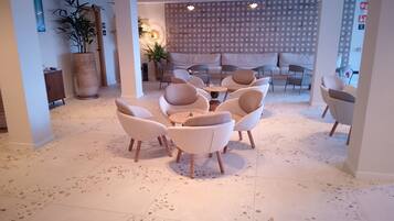 Un interior moderno con una zona de estar que incluye mesas y sillas redondas, una pared decorativa con diseños circulares y una planta grande en maceta.