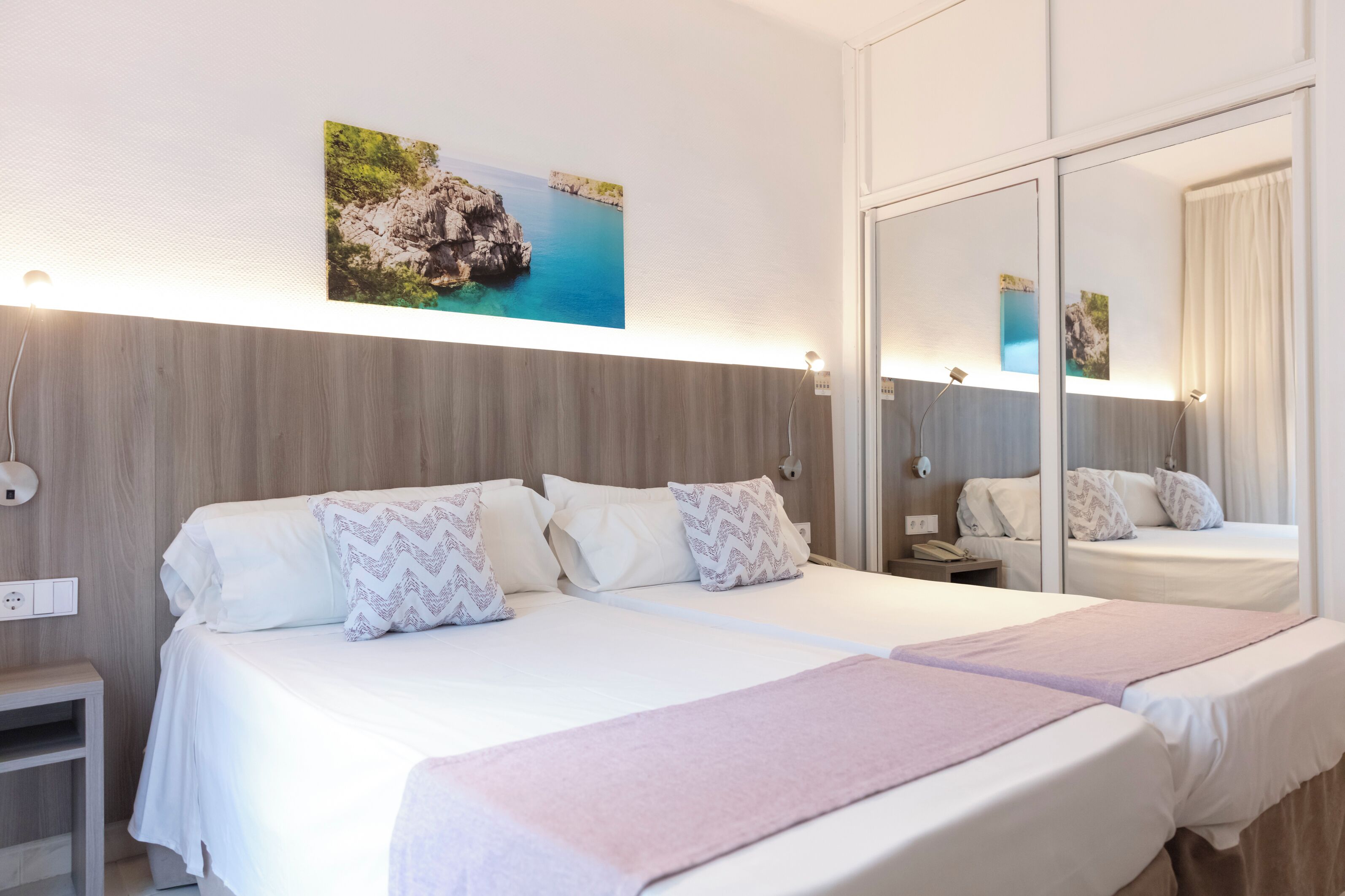 A hotel room with a bed, bedside table, nightstand, and a large mirror.