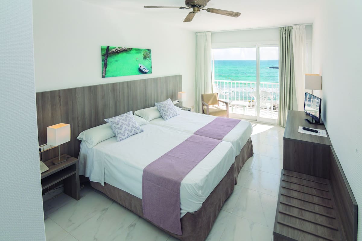 Habitación de hotel con cama, escritorio, silla, televisor y balcón con vista al océano.