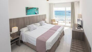 Habitación de hotel con cama, escritorio con computadora, silla, ventana con vista al mar y ventilador de techo.