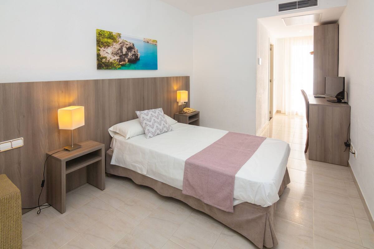 Un dormitorio con cama, lámparas de noche, un escritorio y una silla.