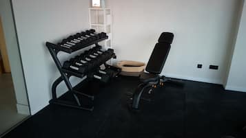Ein Fitnessraum mit einer Langhantelbank, einem Hantelständer und einem kleinen Korb.