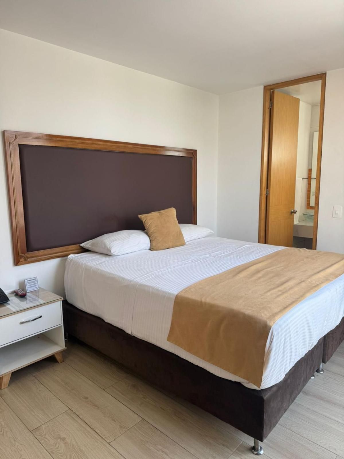 A neatly made bed with a wooden headboard, a bedside table with a lamp, and a mirror on the wall.