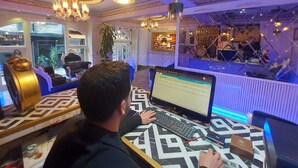 A person working at a desk in a room with patterned flooring, a chandelier, and a view of a hotel in the background. - Leyenda Hotel (Istanbul)
