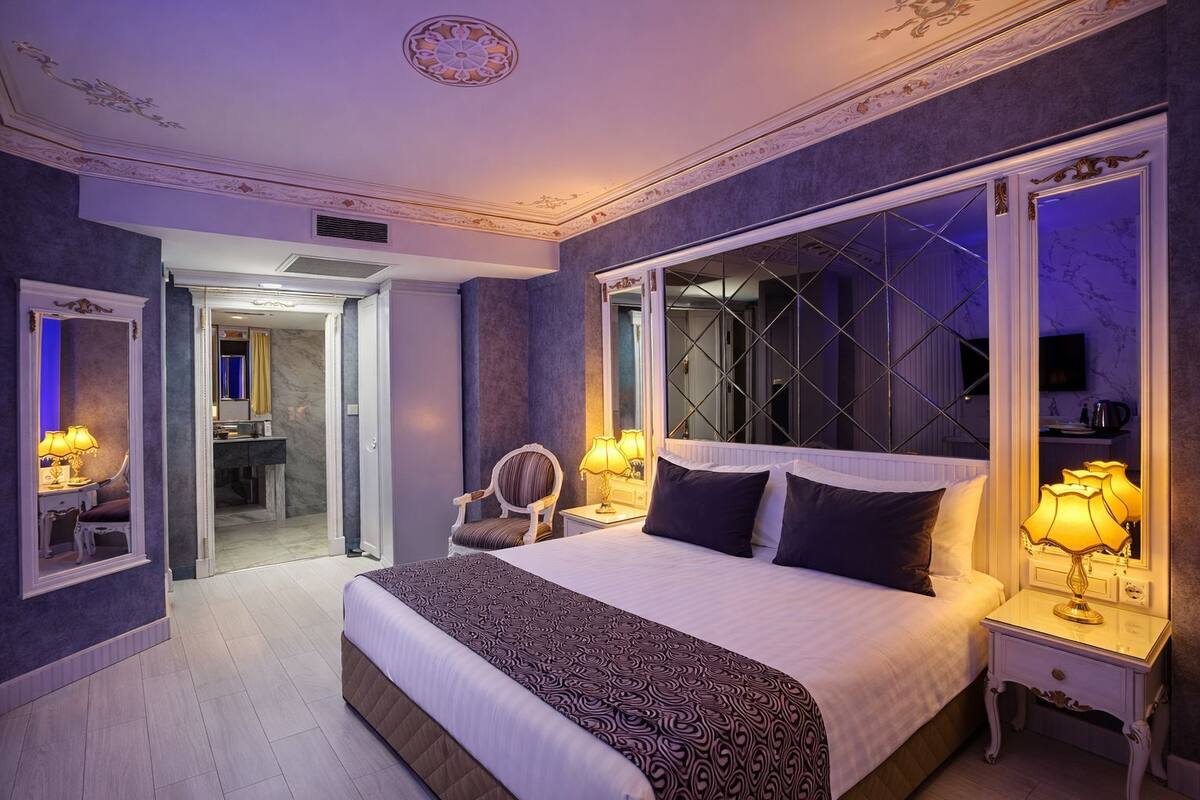 Een ruime slaapkamer met een groot bed, twee nachtkastjes met lampen, een stoel en een spiegel.
