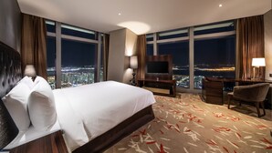 Una habitación de hotel con una cama grande, un escritorio, una silla y un televisor. La habitación tiene ventanas amplias con vistas a la ciudad.