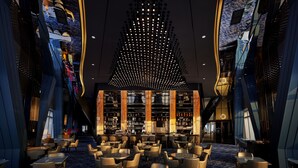 Un moderno vestíbulo de hotel con una zona de bar central, arreglos de asientos y una lámpara de techo distintiva.