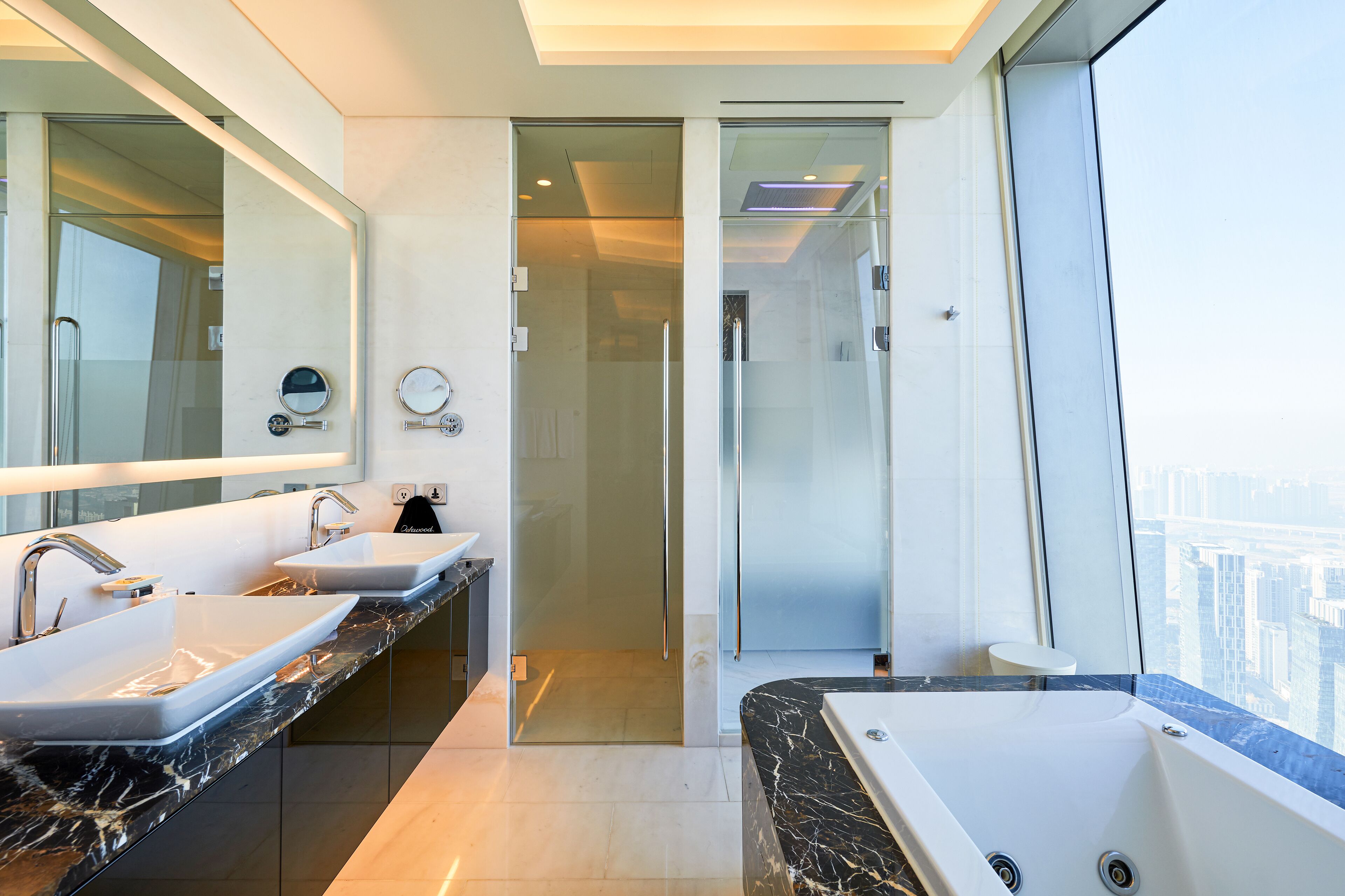 Un baño moderno con dos lavamanos, una bañera grande y un box de ducha de vidrio.