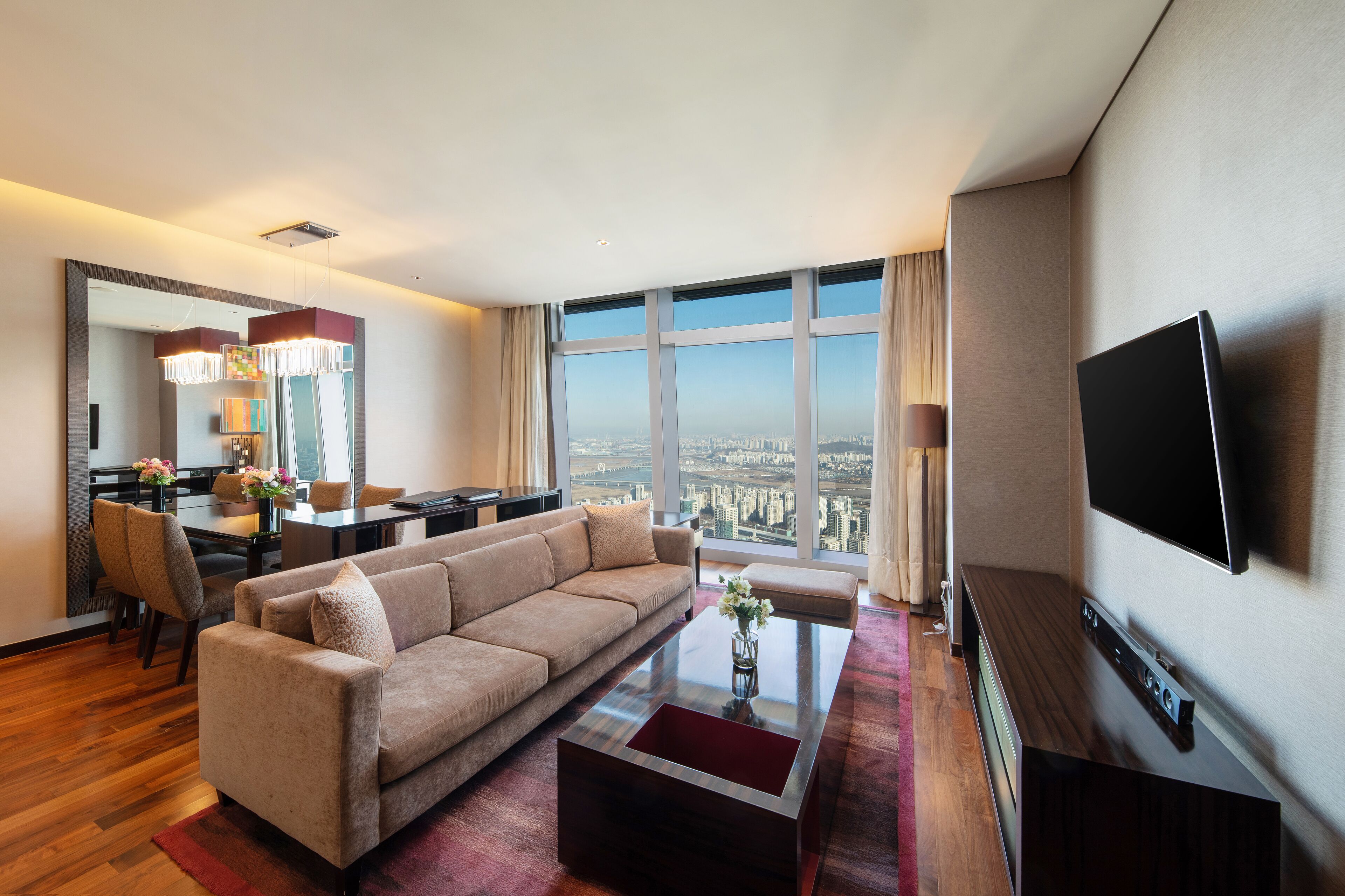 Een moderne hotelkamer met een groot raam, een bank, een eethoek en een flatscreen televisie.