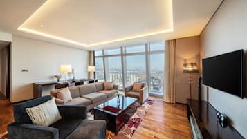 Une chambre d’hôtel moderne dotée d’un grand canapé, d’une table basse, d’un téléviseur à écran plat et offrant une vue sur la ville grâce à de grandes fenêtres.
