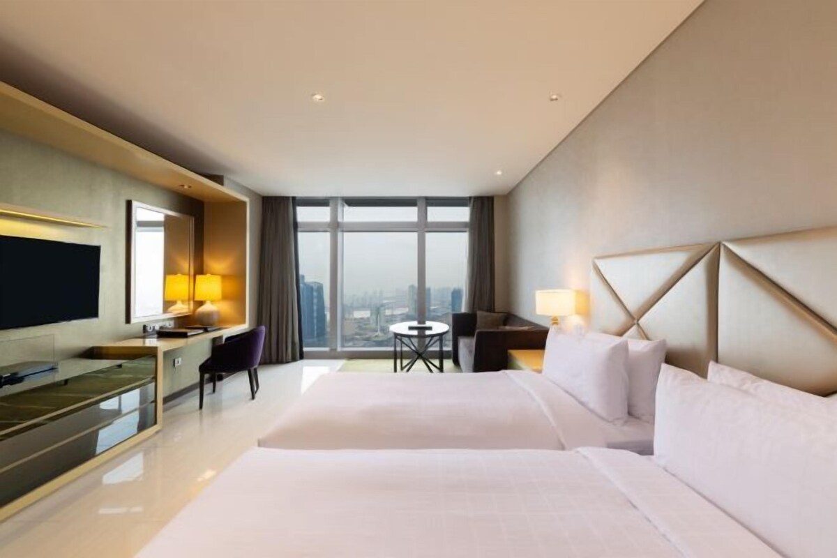 Habitación de hotel con una cama grande, un escritorio, una silla, televisión y vistas a la ciudad.