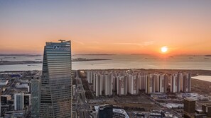 A high-rise building with a prominent sign, surrounded by a dense cluster of residential high-rises, set against a sunset backdrop.