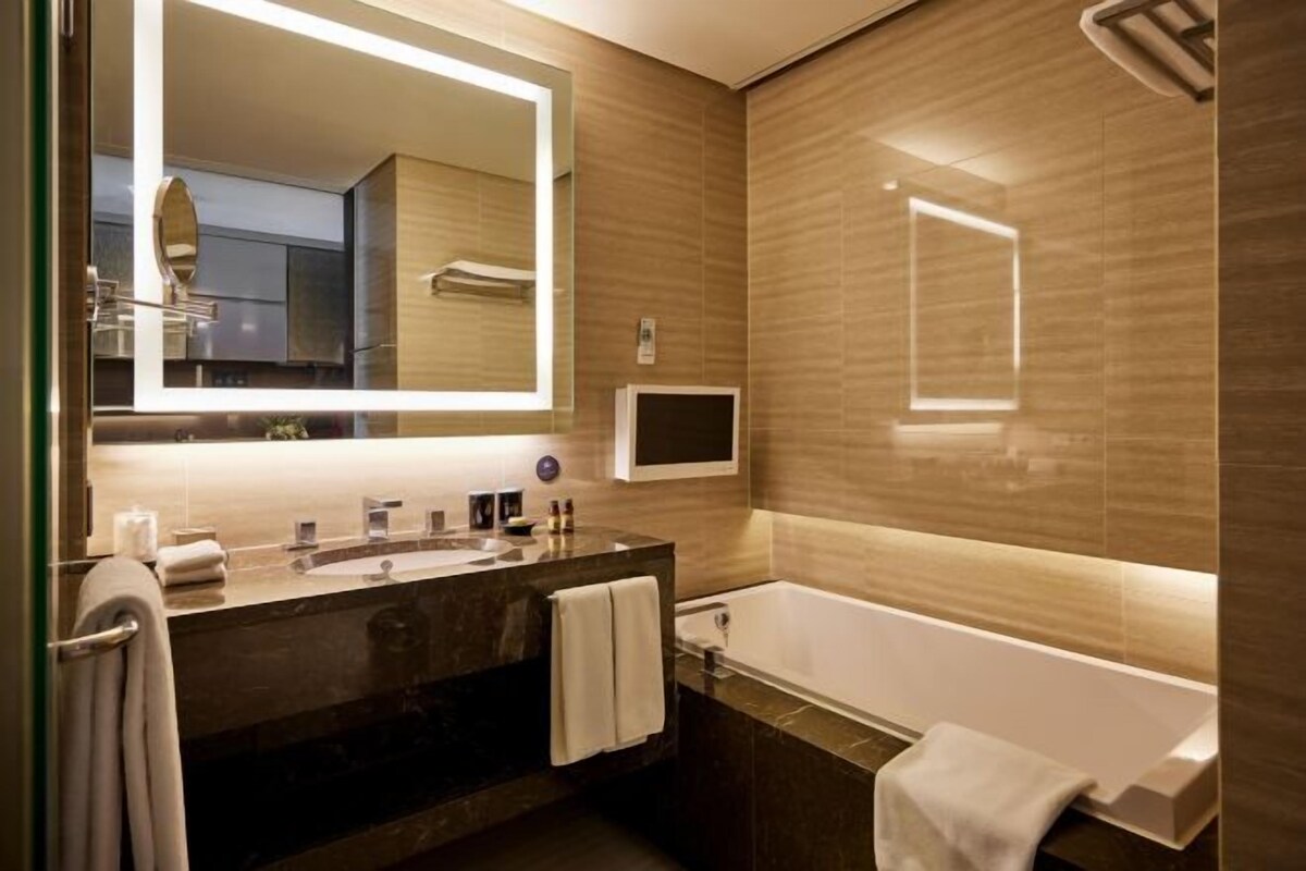 Un baño moderno con un espejo grande, lavamanos dobles, una bañera y un perchero para toallas.