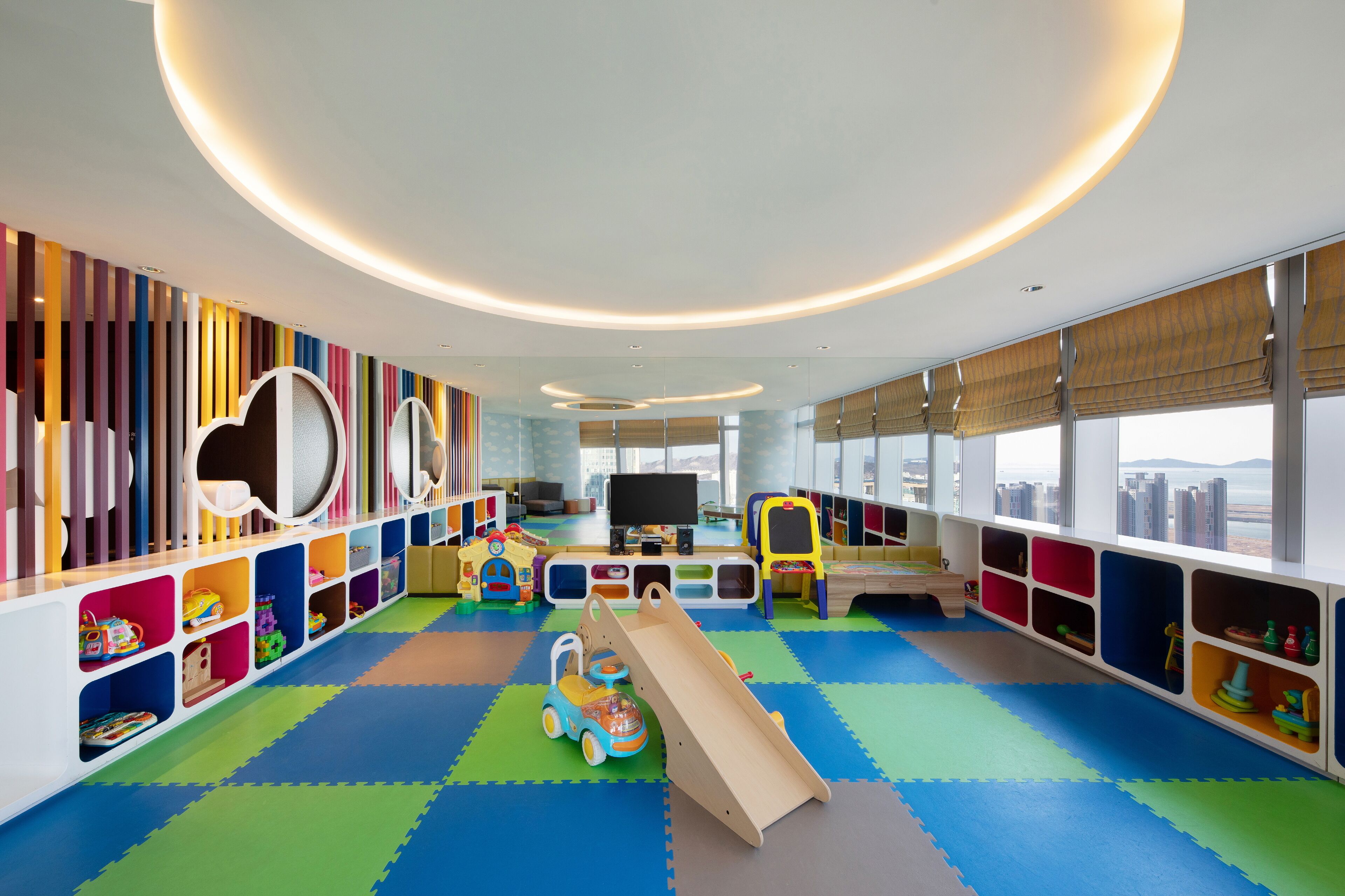 Espaço de recreação infantil com unidades de armazenamento coloridas, um escorrega e uma televisão.
