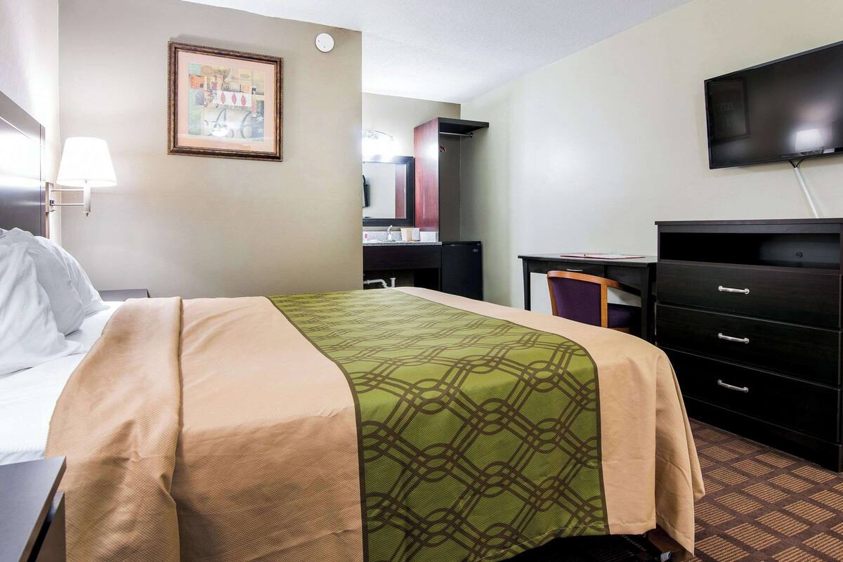 Habitación de hotel con cama, escritorio, cómoda, televisor y un cuadro en la pared.