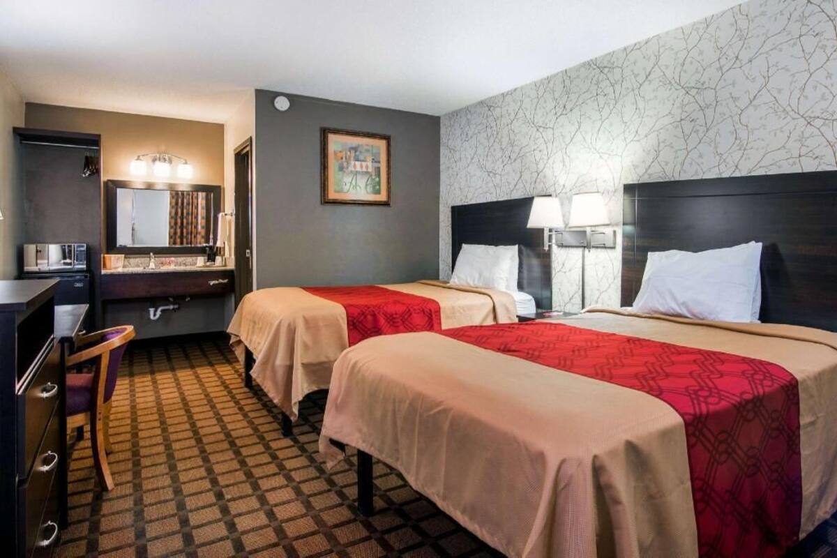 Habitación de hotel con dos camas, un escritorio, una silla, un espejo y un cuadro en la pared.