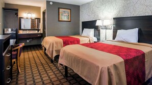 A hotel room with two beds, a desk, a chair, a mirror, and a wall with a patterned wallpaper. - Econo Lodge Selma - Smithfield (Selma)