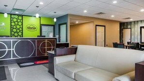 A hotel reception area with a green and blue color scheme, a reception desk, a white sofa, and a dining area in the background. - Econo Lodge Selma - Smithfield (Selma)