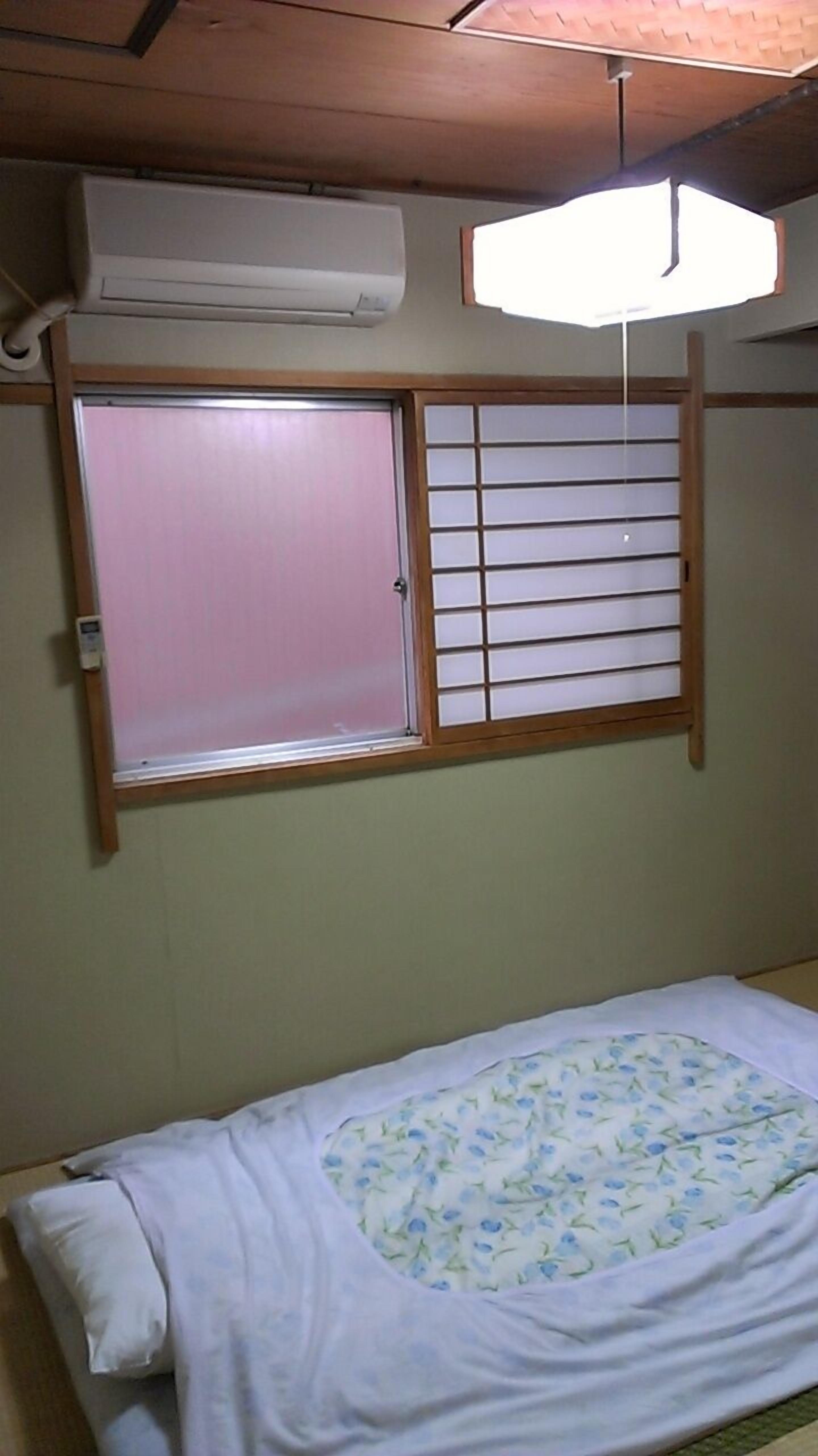 A room with a bed, a window with a wooden frame, and an air conditioning unit on the wall.