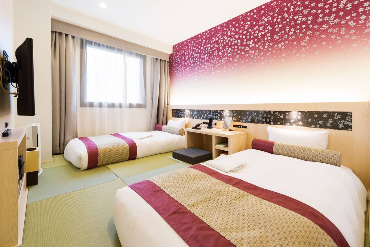 Ein Hotelzimmer mit zwei Betten, einem Schreibtisch und einem Fernseher.