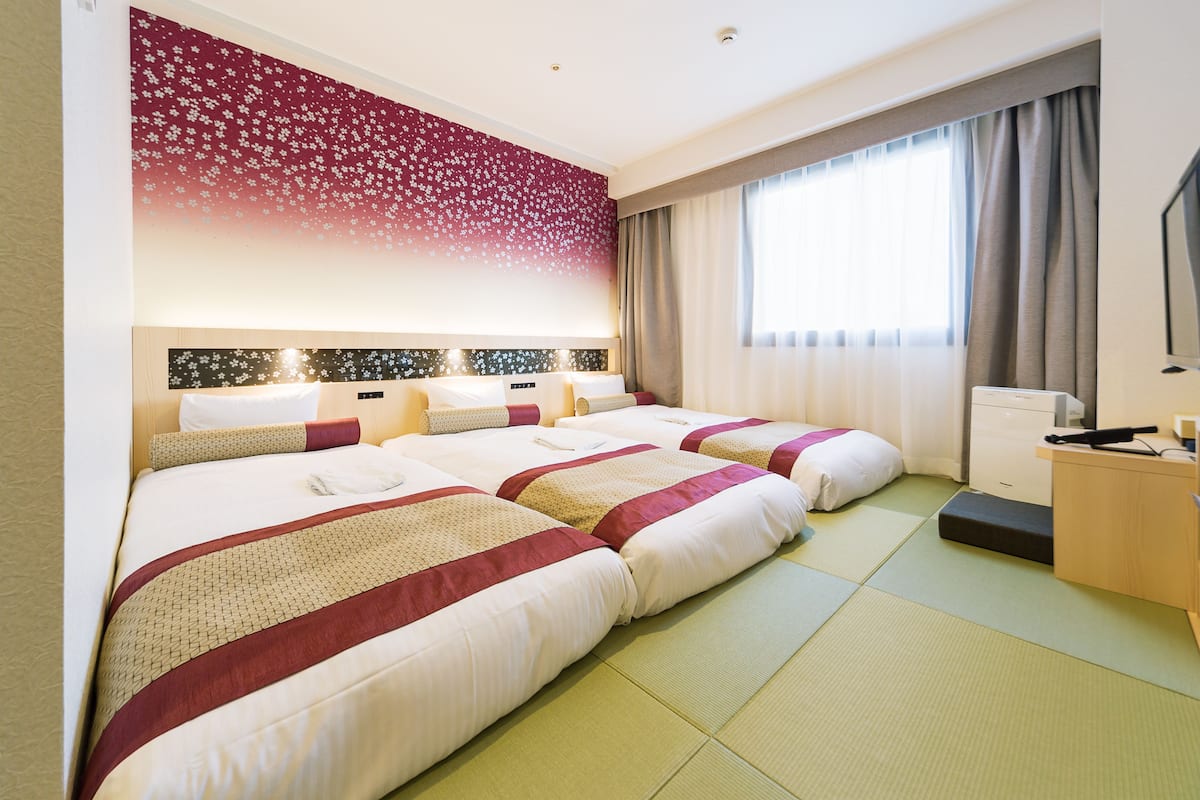 Ein Hotelzimmer mit zwei Betten, einem Schreibtisch und einem großen Fenster mit Vorhängen.