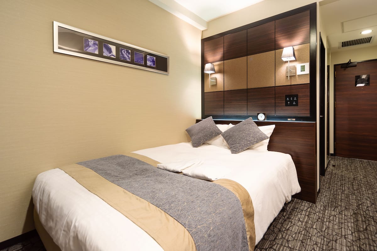 Ein Hotelzimmer mit einem Bett, einem Nachttisch, einer Lampe und einem an der Wand befestigten Bilderrahmen.