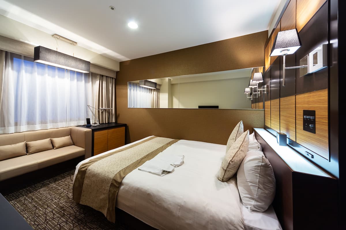 Ein Hotelzimmer mit Bett, einer Couch, einem Schreibtisch, einem Spiegel und einem Fernseher.