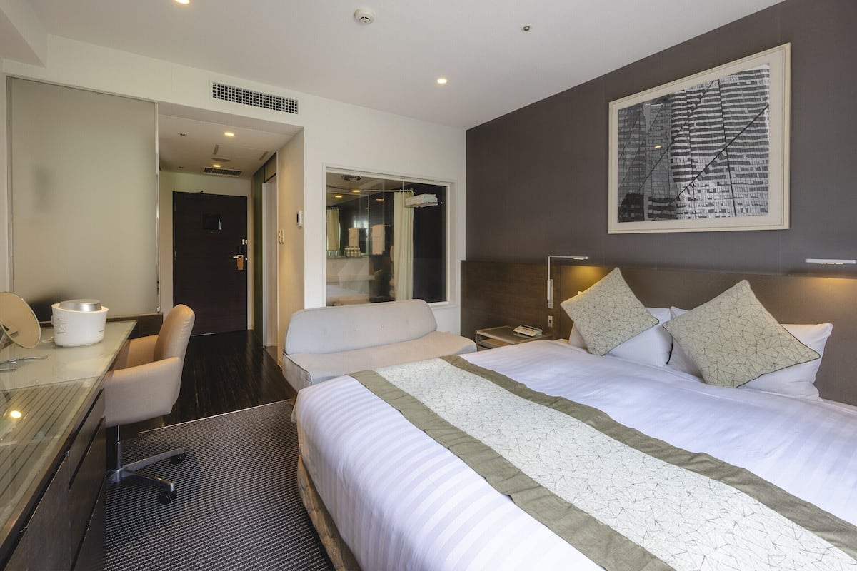Ein Hotelzimmer mit einem großen Bett, einem Schreibtisch mit Stuhl, einem Nachttisch und einem Wandbild.