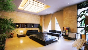 A spacious lobby with a large sectional sofa, a coffee table, and a reception desk. There are potted plants and a bulletin board with information. - KOKO HOTEL Shinjuku Yotsuya (Tokyo)