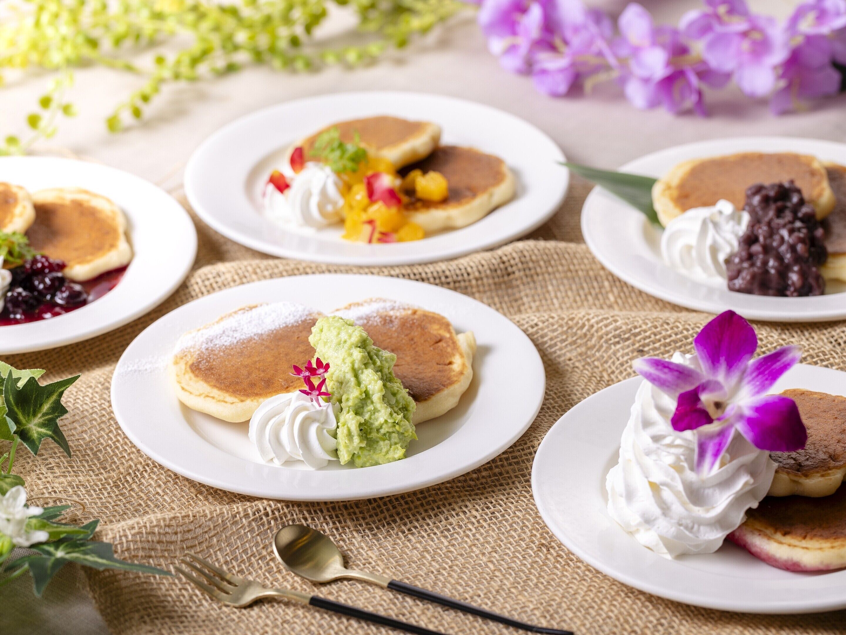 A table with plates of pancakes, some topped with whipped cream and others with fruit and chocolate sauce.