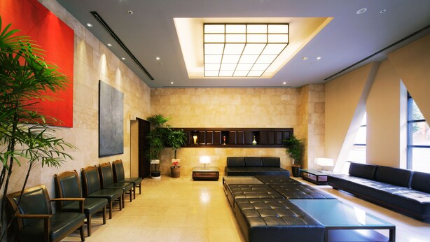 A spacious lobby with a long reception desk, several seating areas, and a large window providing natural light. - KOKO HOTEL Shinjuku Yotsuya (Tokyo)