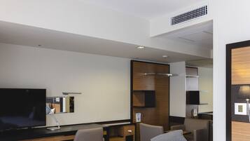 Una habitación de hotel con cama, escritorio, silla, televisor y espejo.