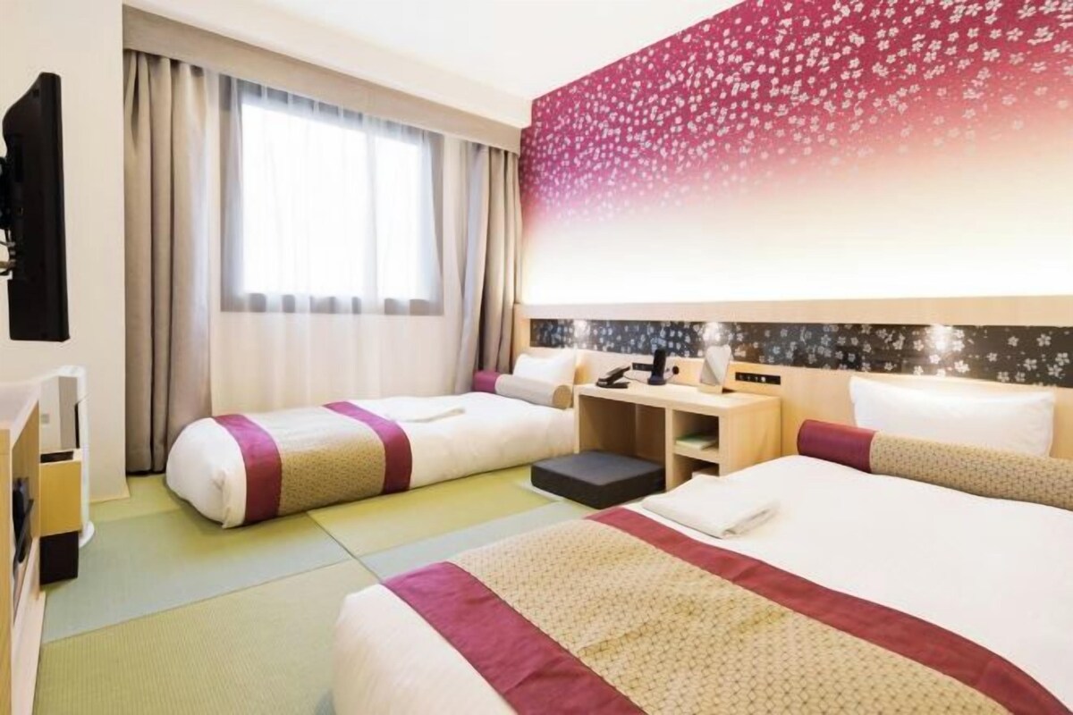 A hotel room with two beds, a desk, a chair, and a large window with curtains.