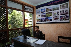 A reception desk with a computer, papers, and a window with a sign reading "Spa & Parlour". - Hotel Peninsula (Pokhara)