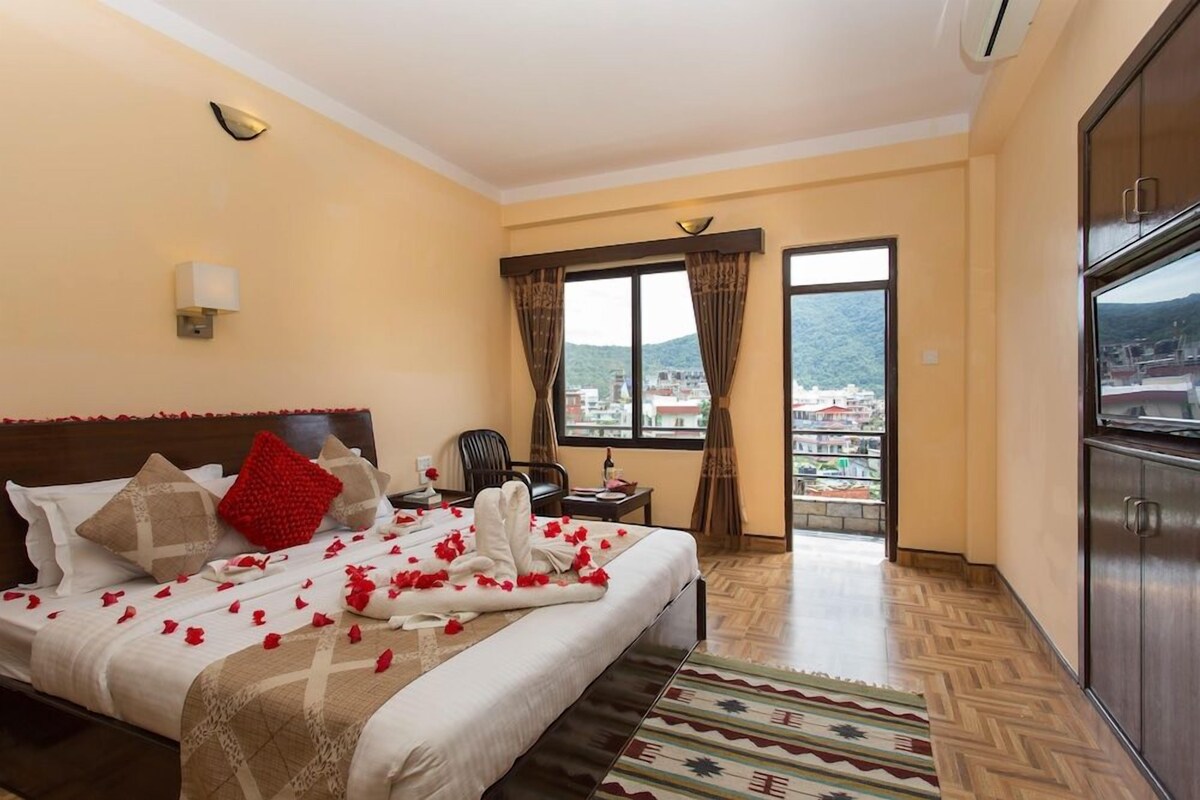 A hotel room with a bed, a desk, a chair, a TV, and a view of the city through the window.
