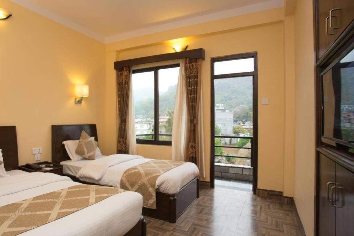 A hotel room with two beds, a balcony with curtains, a TV, and a view of the city.