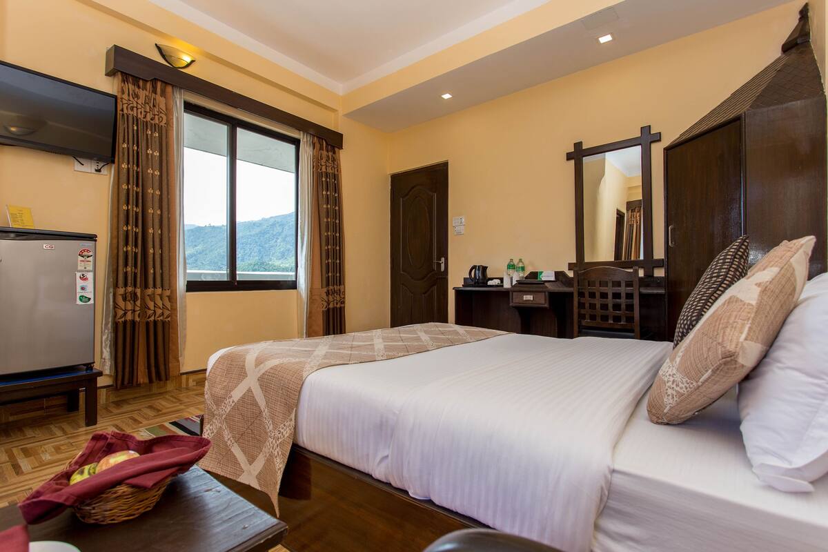 A hotel room with a bed, a desk, a chair, a TV, and a window with curtains.
