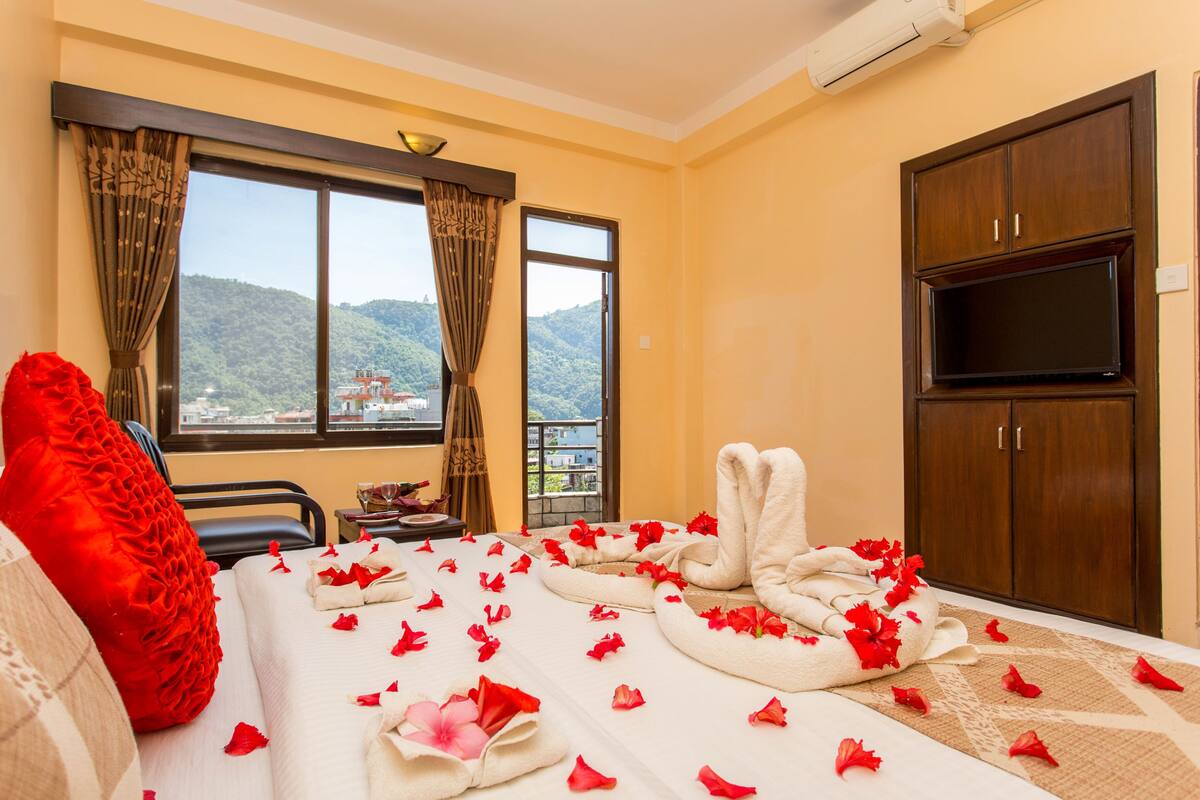 A hotel room with a bed, a red pillow, a TV, and a view of a mountain.