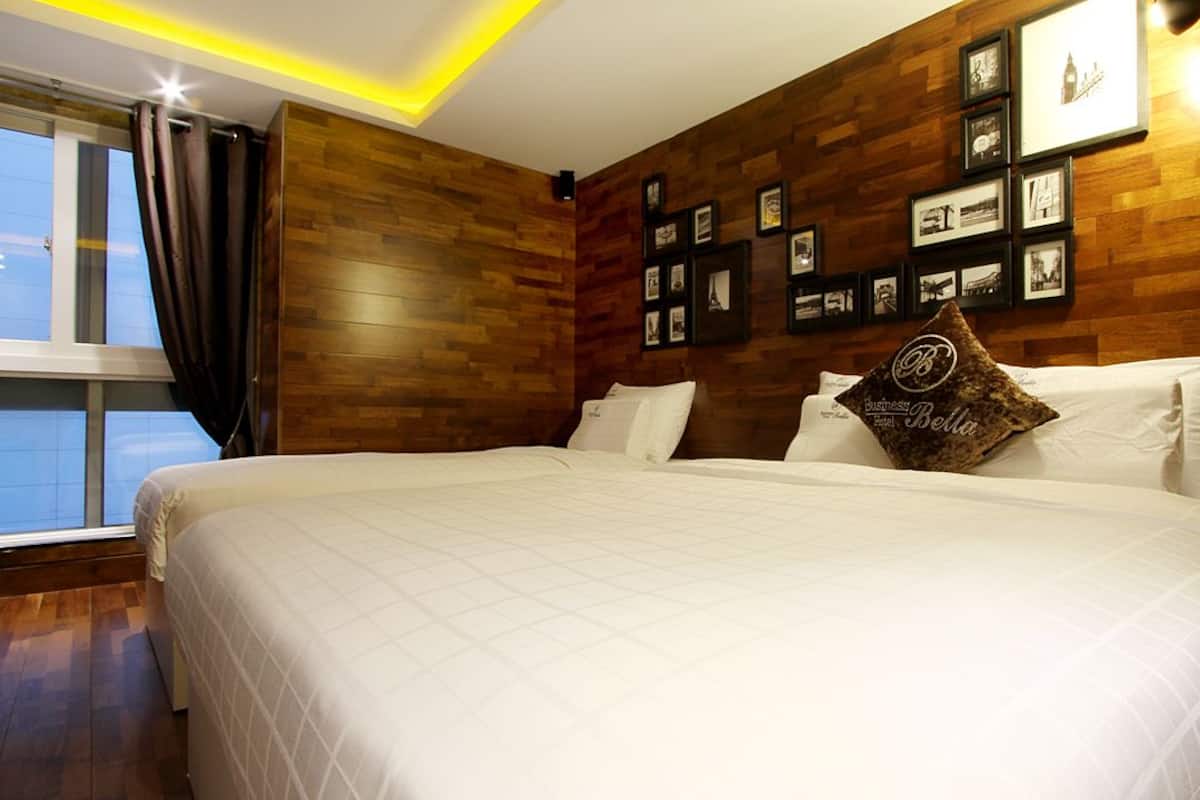 A hotel room with a large bed, wooden panel walls, framed pictures, and a window with curtains.