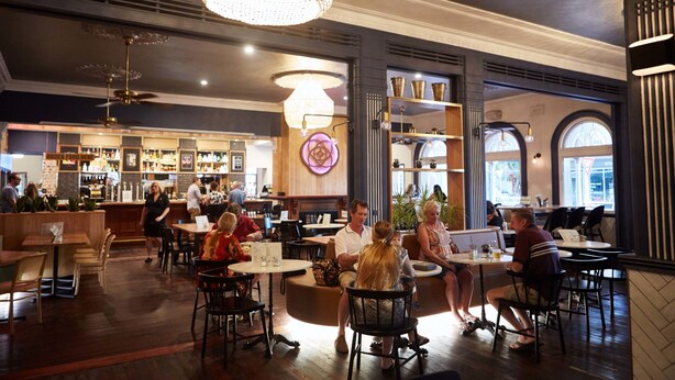 A restaurant with round tables and booths, a bar area, and a chandelier. - Rose Hotel & Motel (Bunbury)