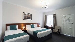 A hotel room with two beds, a wooden headboard, a desk, a chair, a window with curtains, and a door. - Rose Hotel & Motel (Bunbury)