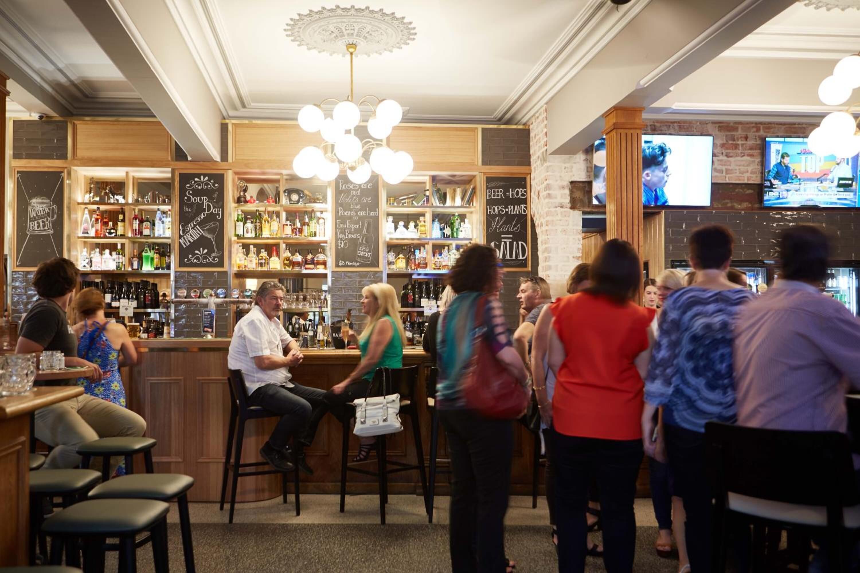 A bar with wooden shelves stocked with bottles, a chalkboard menu, and a television screen.