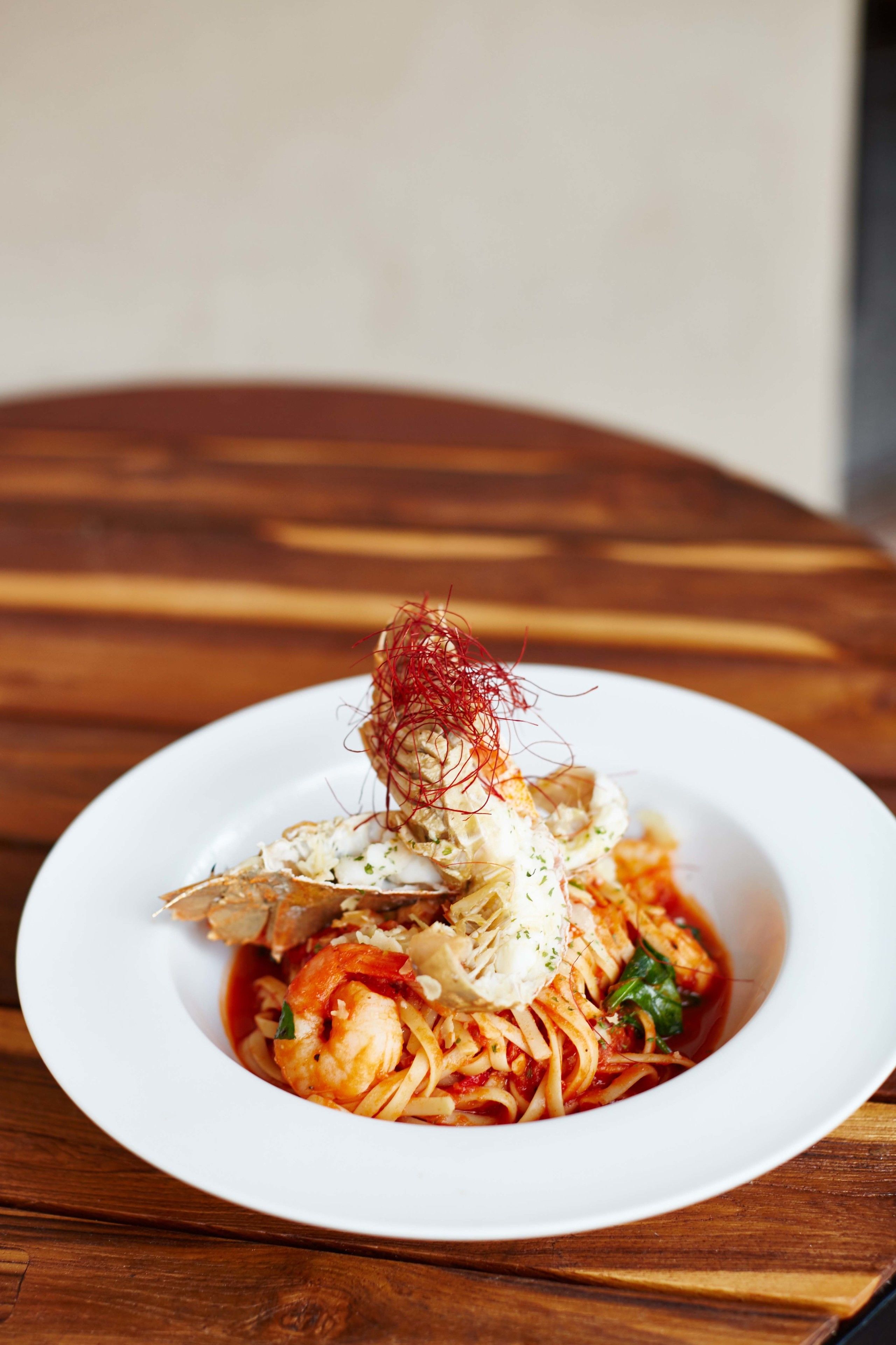 Plat de pasta amb gambes, decorat amb hebra vermella i formatge ratllat, presentat sobre un plat blanc.