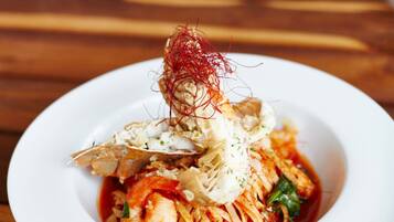 Plat de pasta amb gambes, decorat amb hebra vermella i formatge ratllat, presentat sobre un plat blanc.
