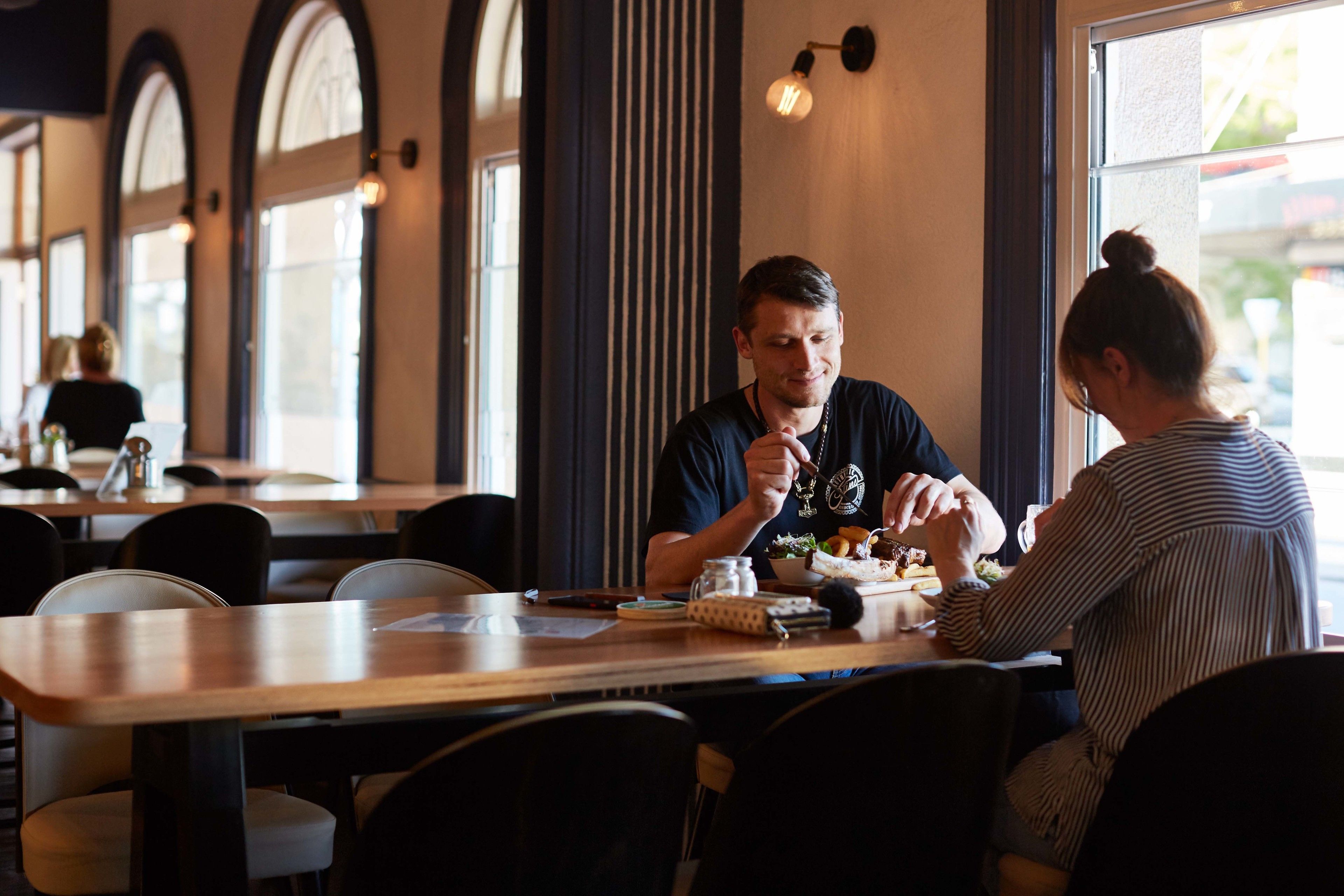 A restaurant with wooden tables and chairs, large windows, and a modern interior design.