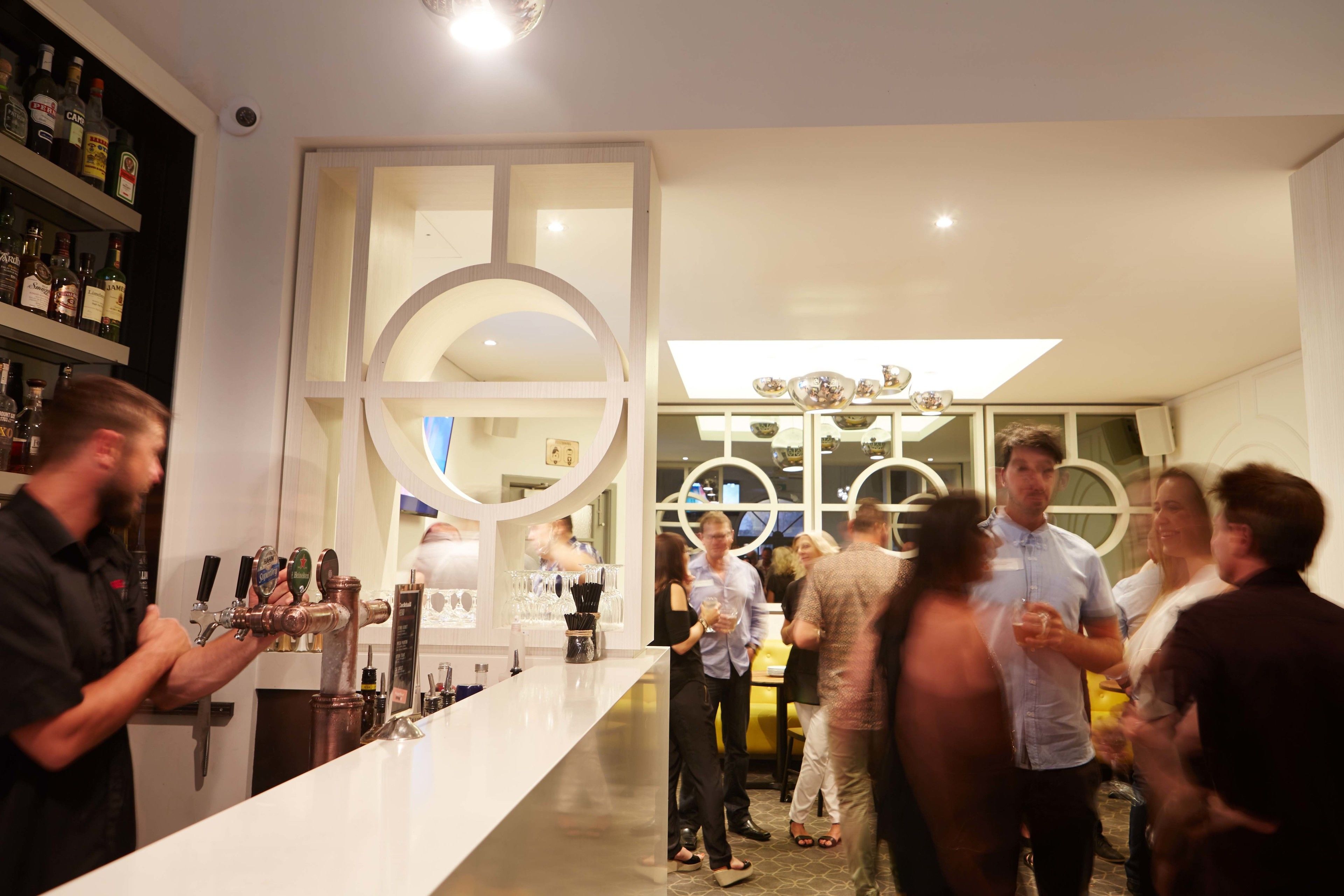 A bar area with multiple taps and a white counter. There are people gathered around, some holding drinks.