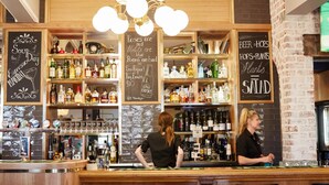 A bar area with shelves of liquor bottles, a chalkboard with writing, and a brick wall. - Rose Hotel & Motel (Bunbury)