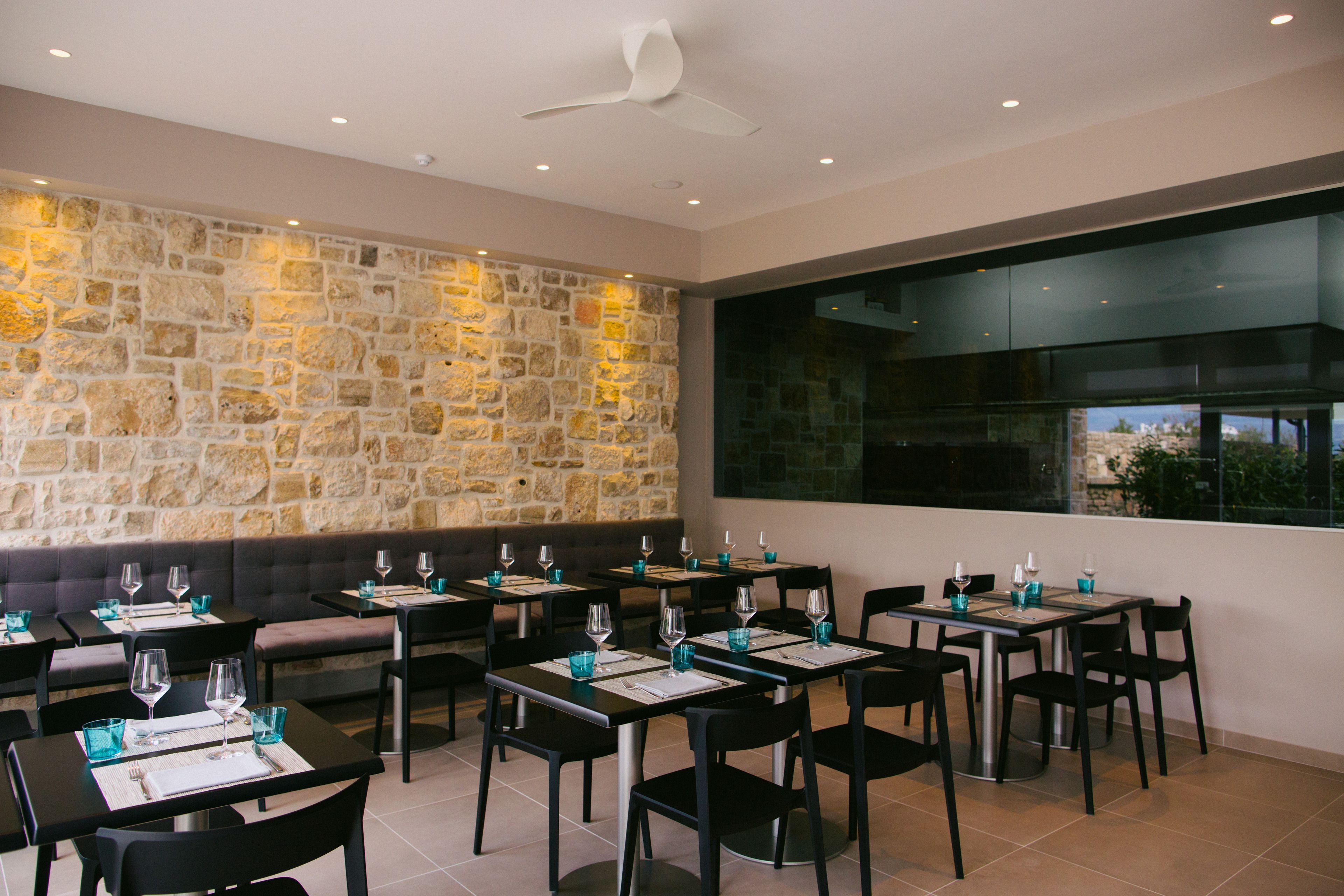 A restaurant with stone walls, black chairs, and tables set with wine glasses and menus.